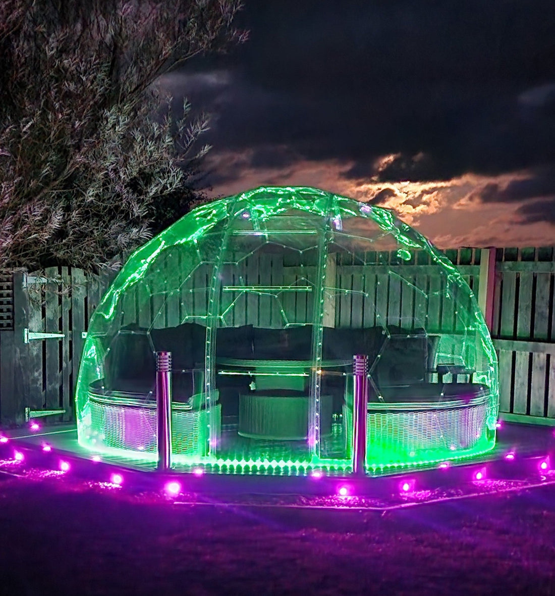 A GeoDomeX dome lit with green and purple LED lights at night